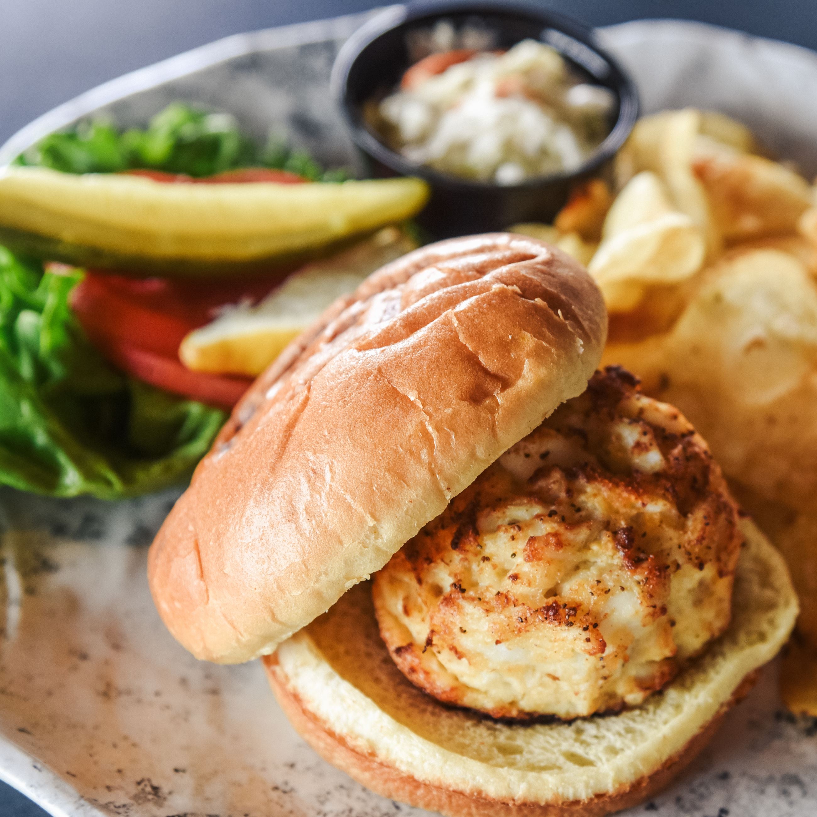 Crab cake sandwich with chips and a pickle