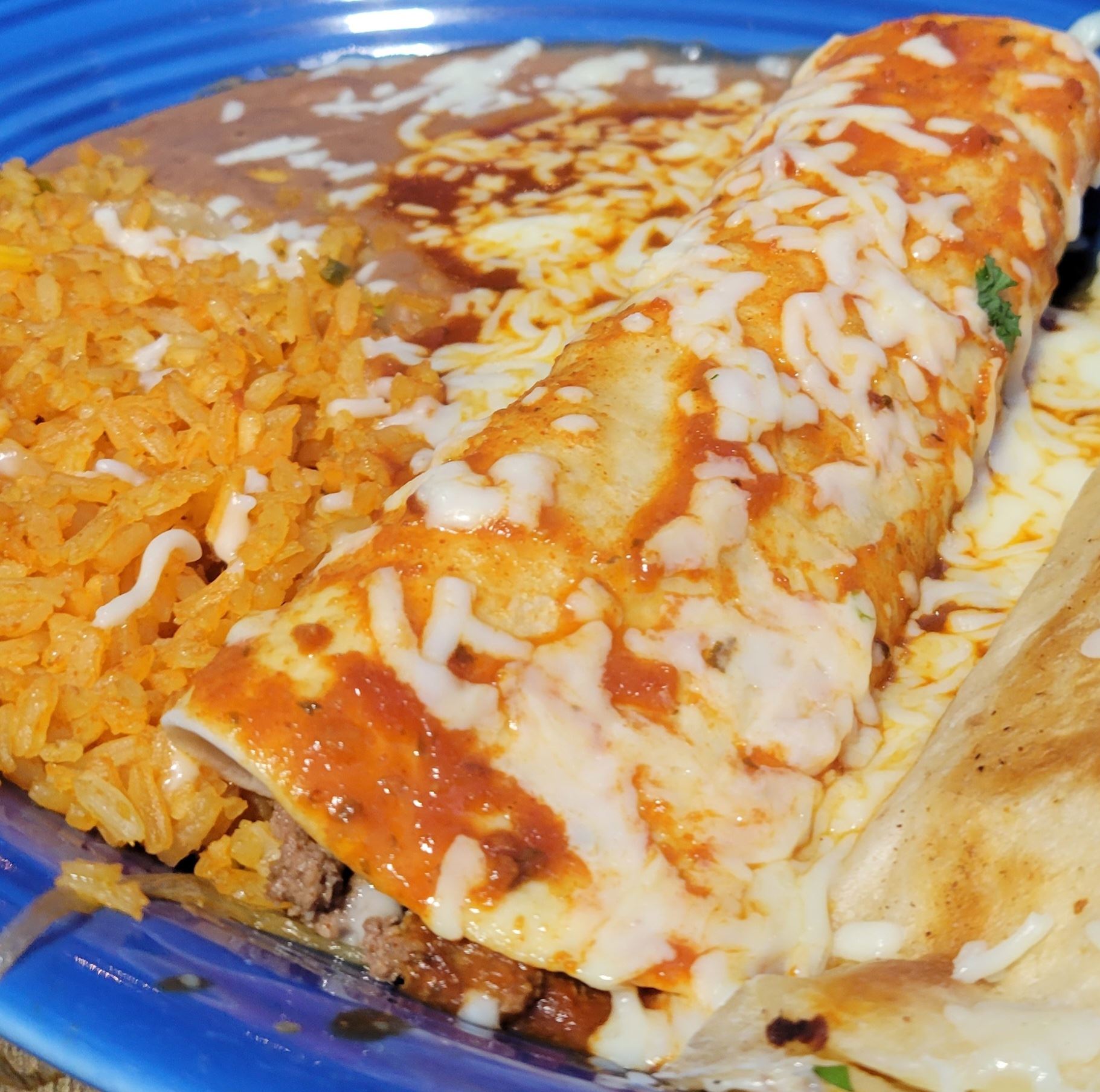 Burrito covered in enchilada sauce and chees with a side of rice