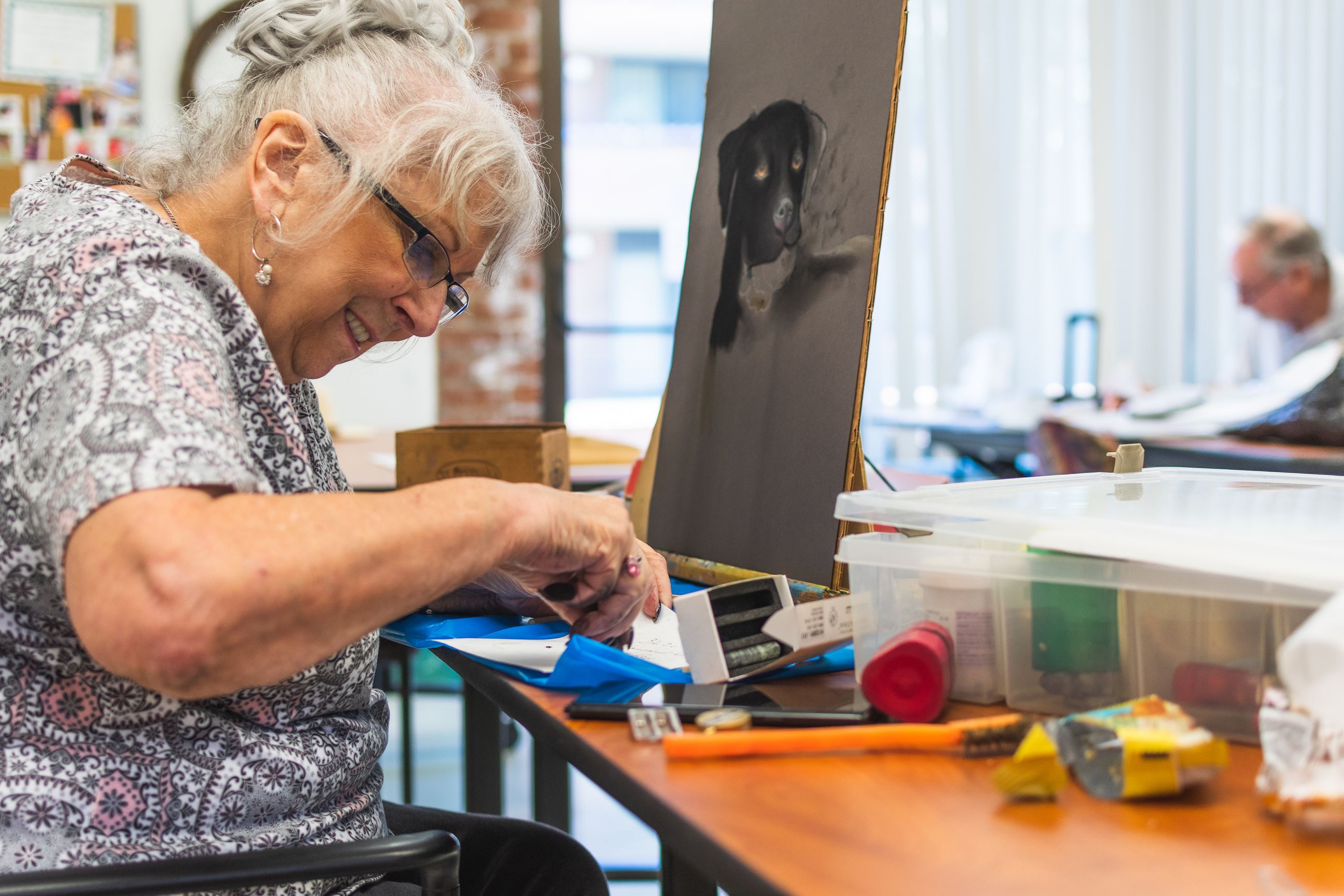 Woman sitting at an easel creating a black dog portrait