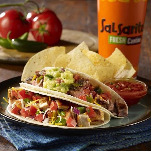 Chicken and steak tacos with drink cup and tomatoes in the background