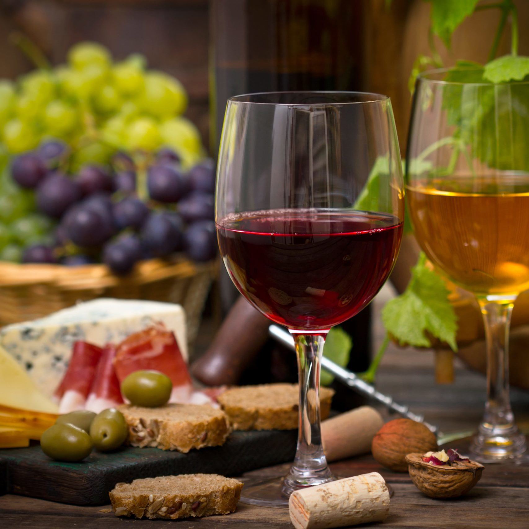 Glass of red and glass of white wine with grapes, cheese, olives and meats