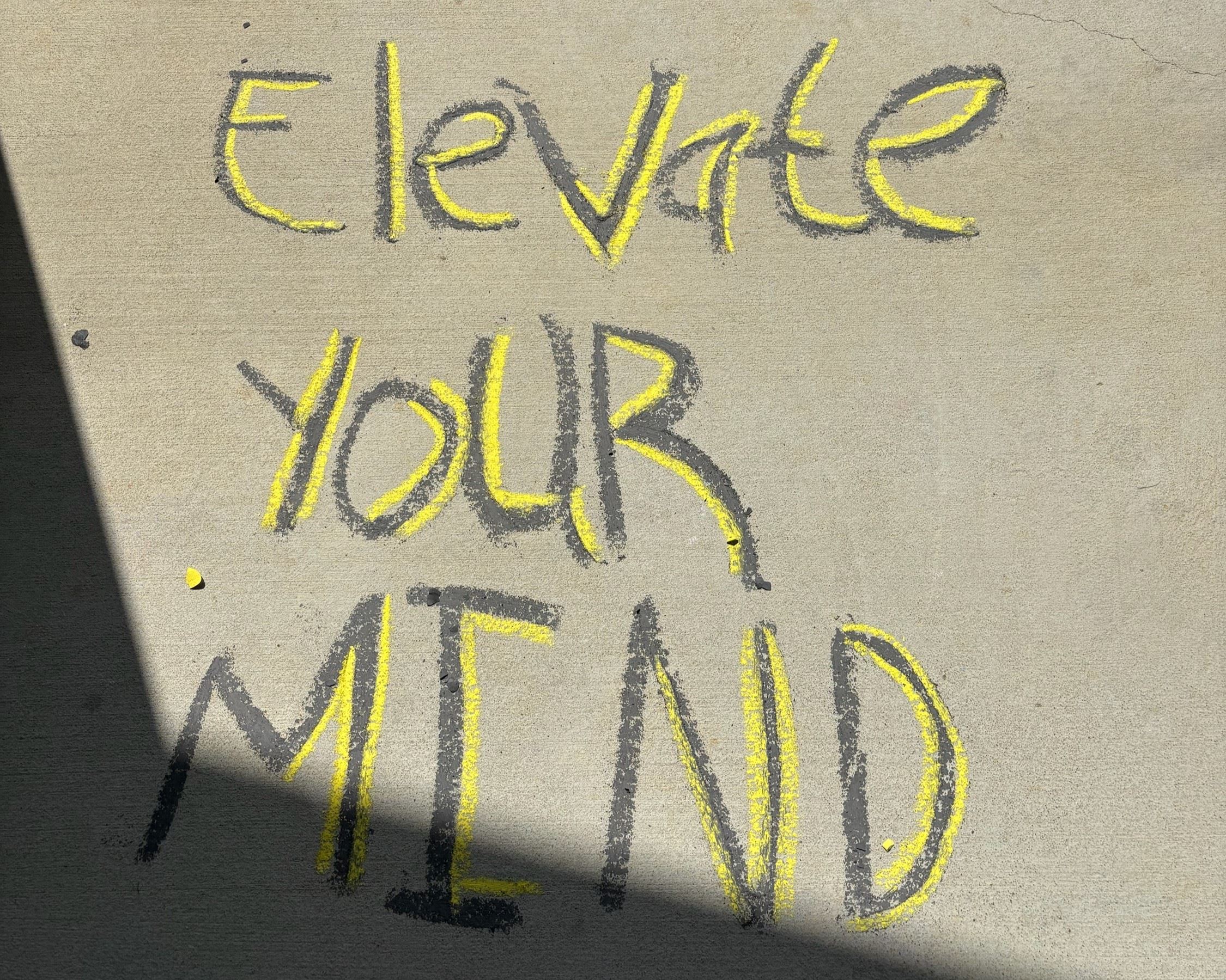 4 students kneeling on the sidewalk writing and drawing with chalk.