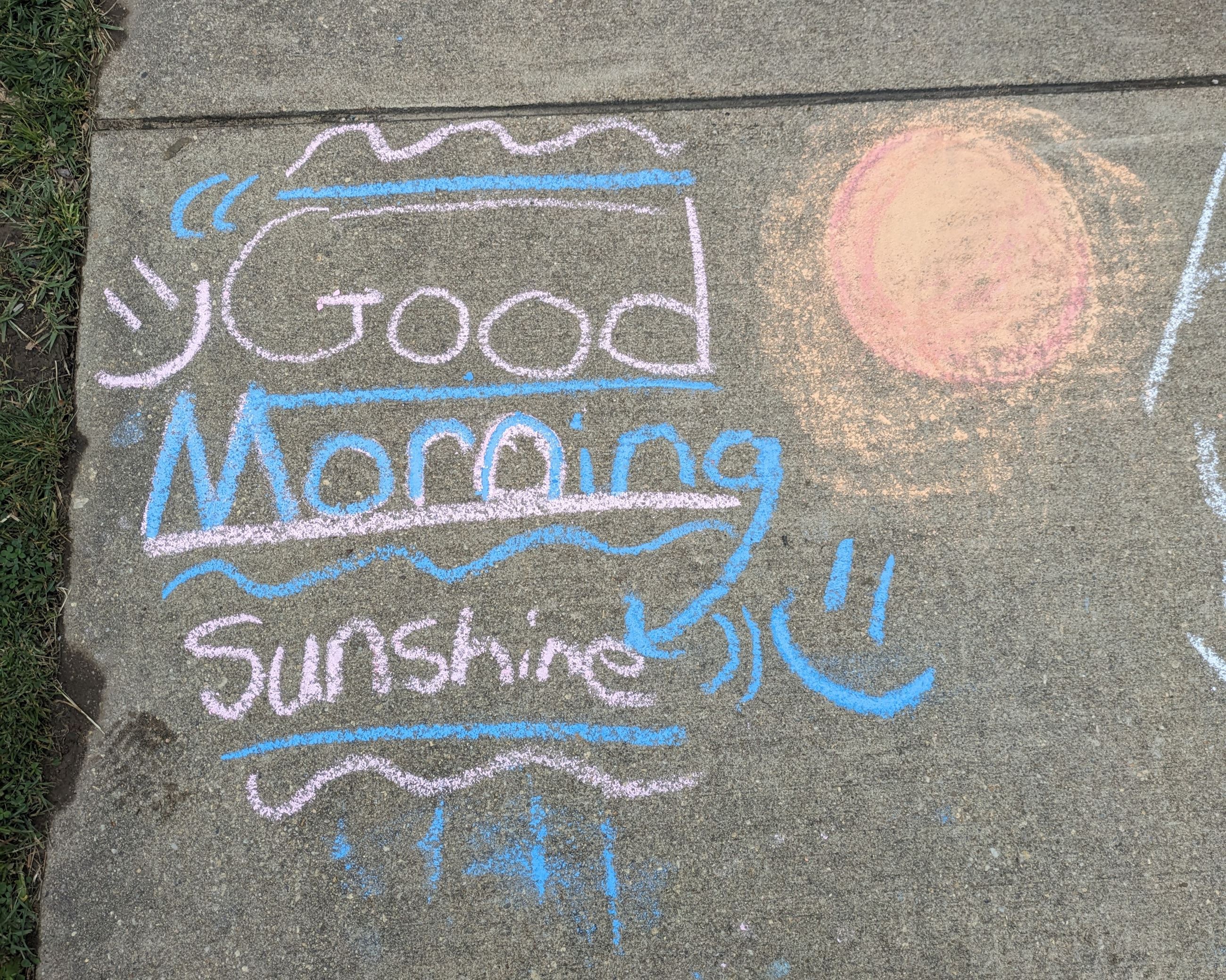 Multicolored sidewalk chalk art of a sun with text "Good morning sunshine."