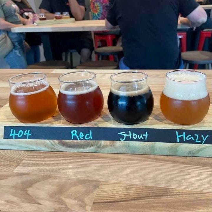 four glasses of varieties of beer arranged on a wooden flight that are labeled 