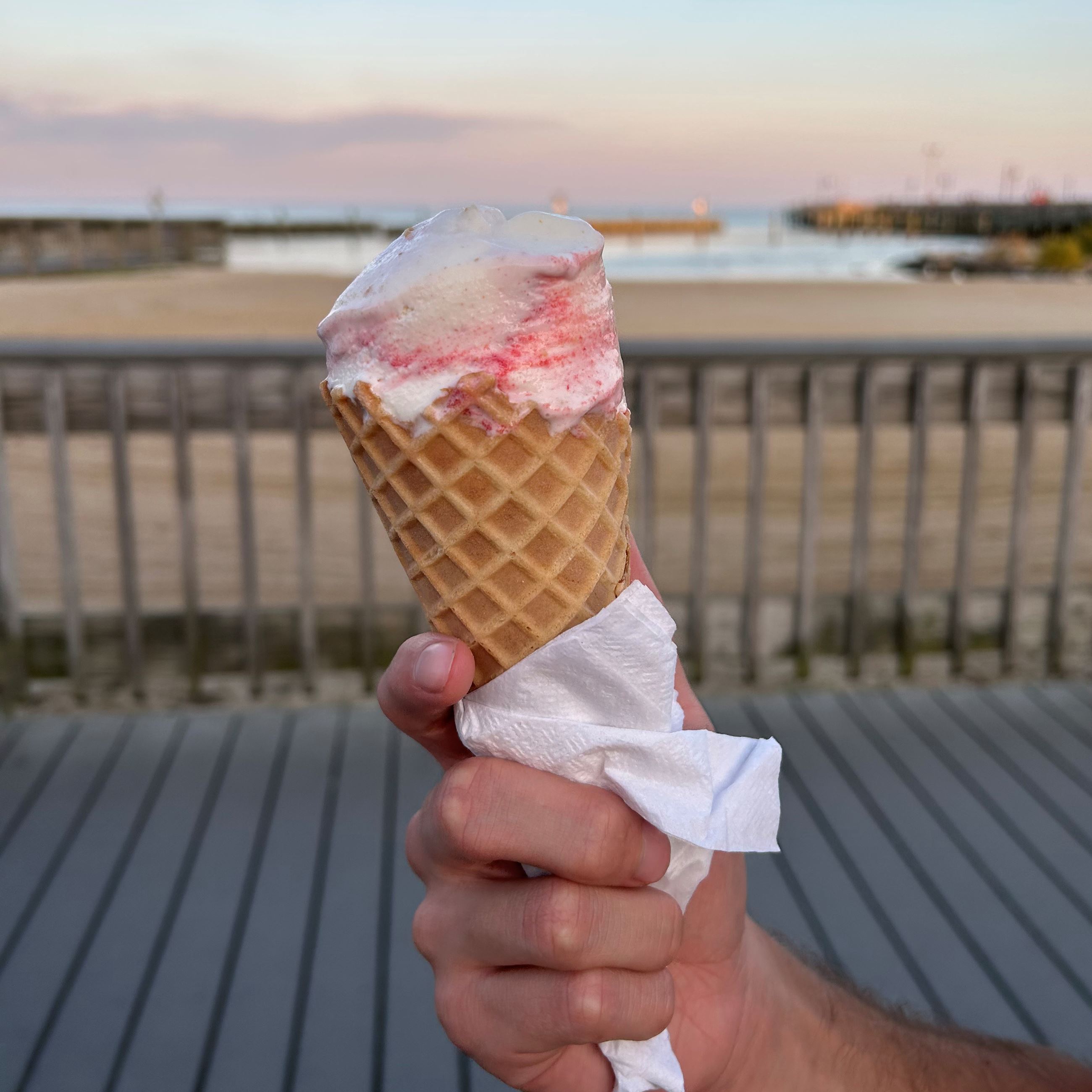 Pink ice cream on a cone in front of the boardwalk and bay  Opens in new window